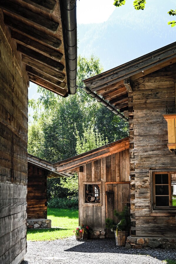 A rustic wooden cabin with a stone foundation, a wooden porch, and a window overlooking a lush green landscape.