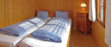 A wooden cabin room with two beds, a nightstand, and a window with curtains.