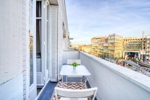 A balcony with a table and chair, a potted plant, and a view of a cityscape with buildings and a bridge. - Apartment 'Terrace and Comfort – Austerlitz' with Balcony and Wi-Fi (Paris)