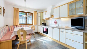 A kitchen with a dining area, wooden cabinets, a stove, and a television. - Apartment 'Vergissmeinnicht 14' with mountain view, private terrace and Wi-Fi (Santa Valburga)