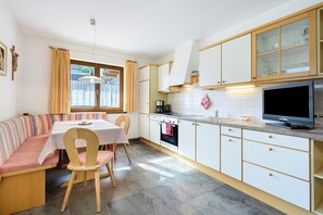 Une cuisine avec un coin repas, des meubles de rangement en bois, une cuisinière et un téléviseur.