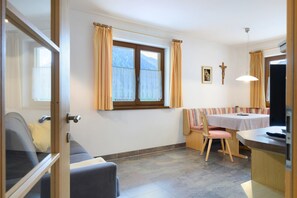 Une pièce comprenant un lit, une table, une chaise, une fenêtre avec des rideaux, un crucifix et un tableau accroché au mur.