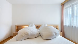 A bed with white bedding, a wooden headboard, and a nightstand with a lamp. - Apartment 'Vergissmeinnicht 14' with mountain view, private terrace and Wi-Fi (Santa Valburga)