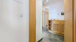A hallway with a wooden door, a wall-mounted light switch, and a kitchen area with wooden cabinets and a tiled floor. - Apartment 'Vergissmeinnicht 14' with mountain view, private terrace and Wi-Fi (Santa Valburga)
