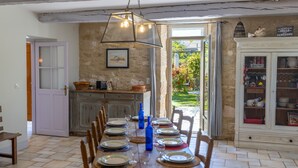 Uma sala de jantar com mesa posta para seis lugares, parede de pedra, armário de madeira e porta que dá para o exterior.