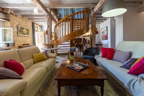 Ein Wohnzimmer mit einer Holztreppe, einem Sofa, einem Couchtisch und einem Bücherregal.