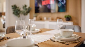 A dining table set with plates, bowls, glasses, and cutlery, with a television mounted on the wall in the background. - Urban Haven Central Retreat | Free Parking | 16PPL (Sheffield)