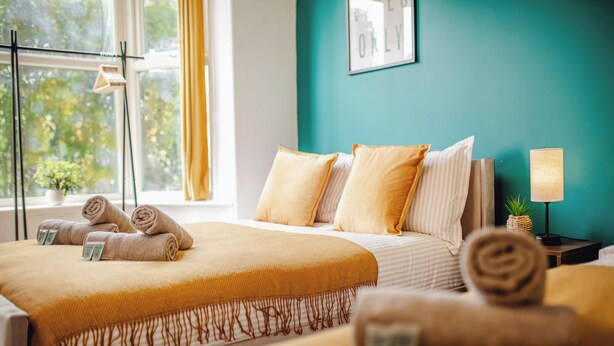 A bedroom with two beds, a window with curtains, a bedside table with a lamp, and a wall with a framed picture. - Urban Haven Central Retreat | Free Parking | 16PPL (Sheffield)