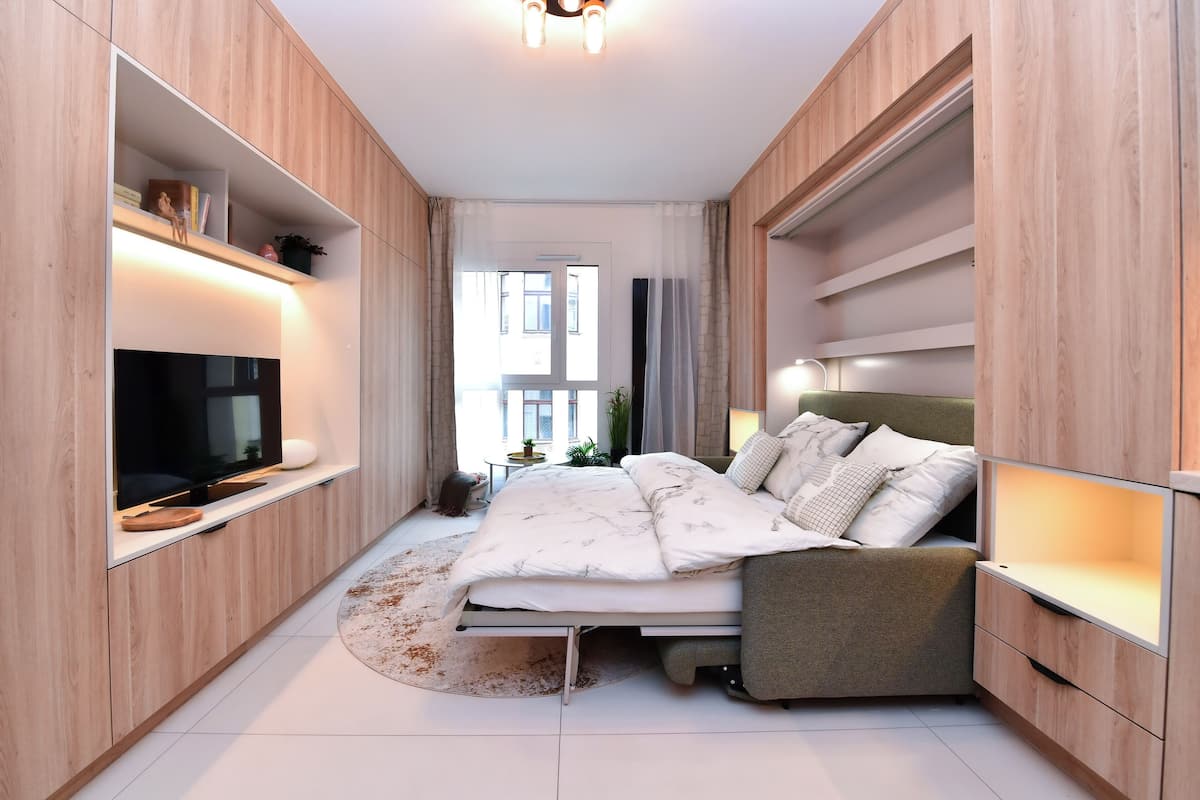 Un dormitorio moderno con cama, televisor integrado y estanterías de madera.