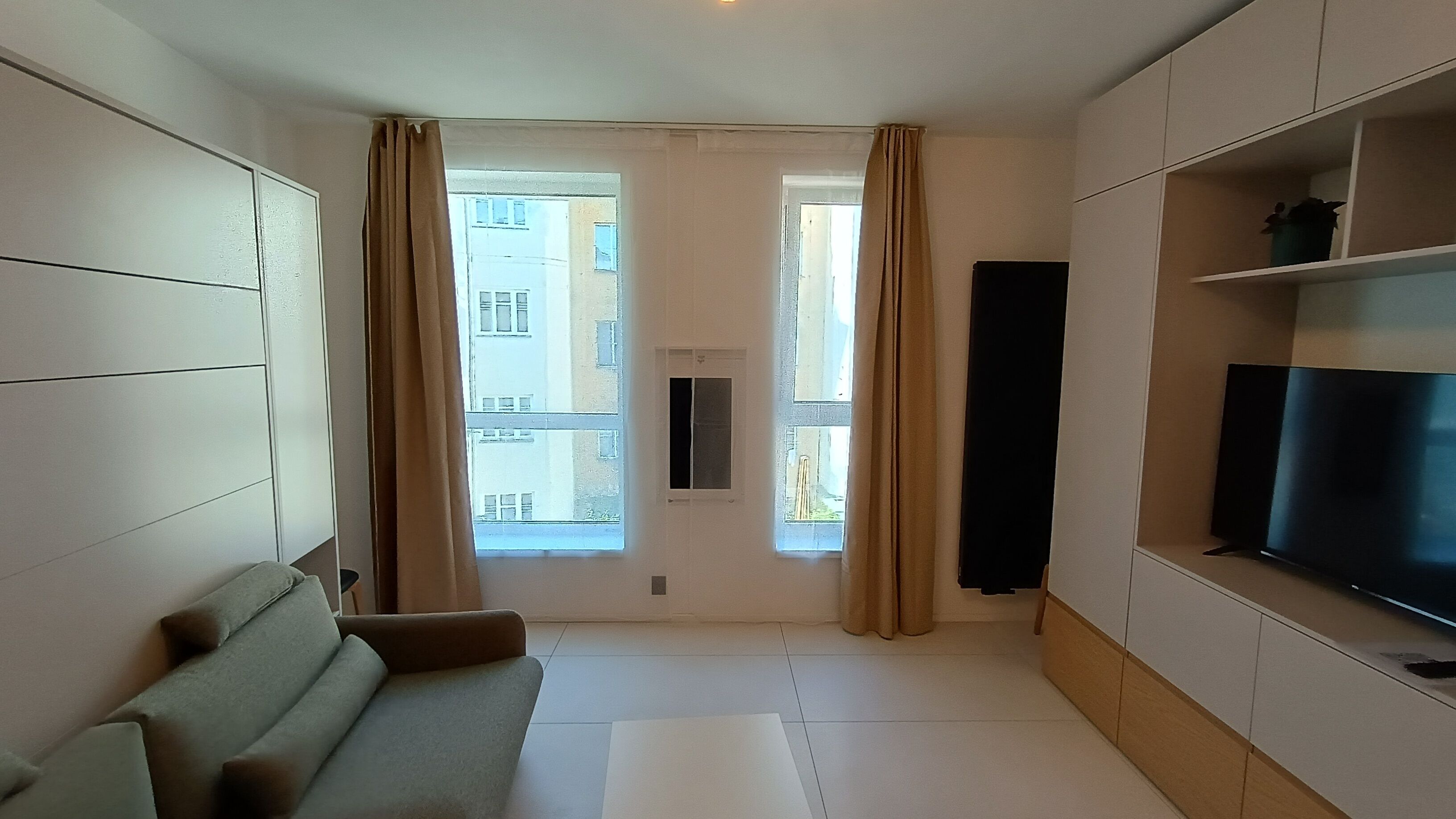 Un salon moderne avec un canapé, un téléviseur à écran plat et une fenêtre avec des rideaux.