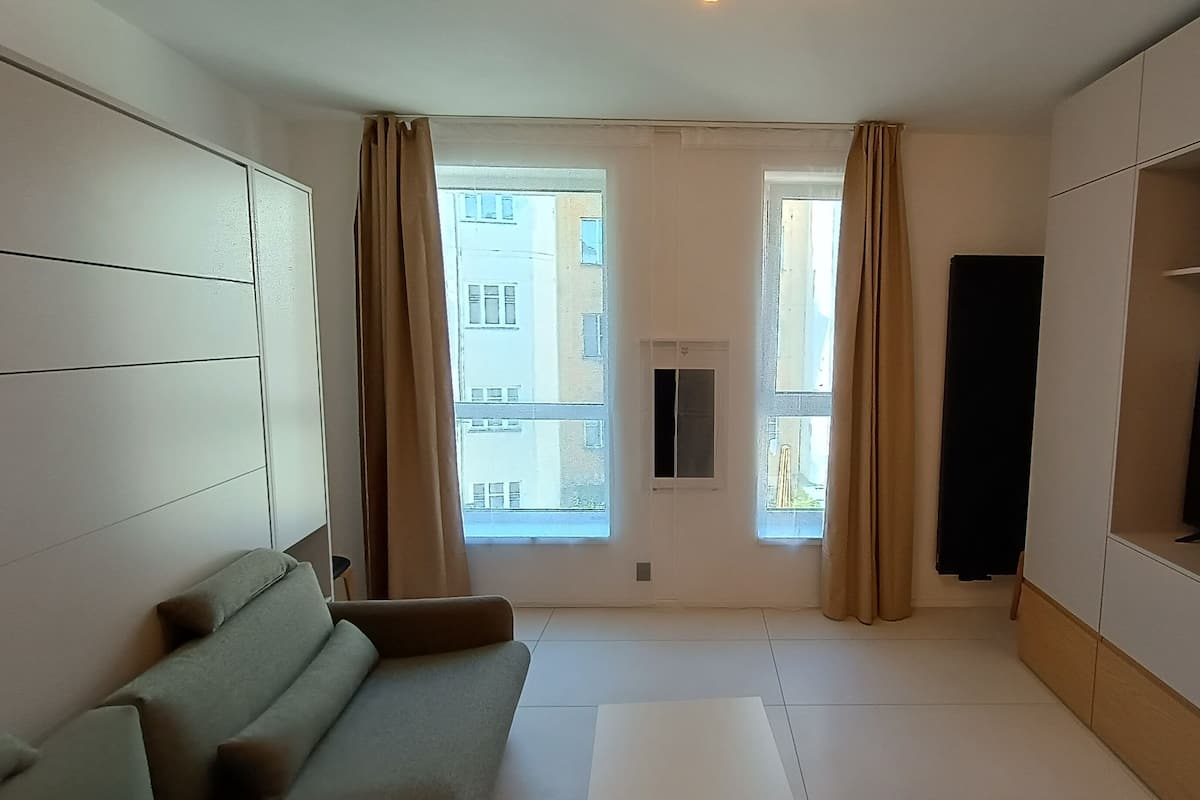 Una sala de estar moderna con un sofá, un televisor de pantalla plana y un ventanal con cortinas.