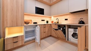 A modern kitchen with wooden cabinetry, a built-in microwave, a dishwasher, and a washing machine. - Krymská Studios  (Prague)