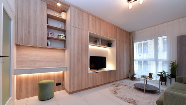 A modern living room with built-in shelves, a flat-screen TV, a round coffee table, and a green ottoman. - Krymská Studios  (Prague)