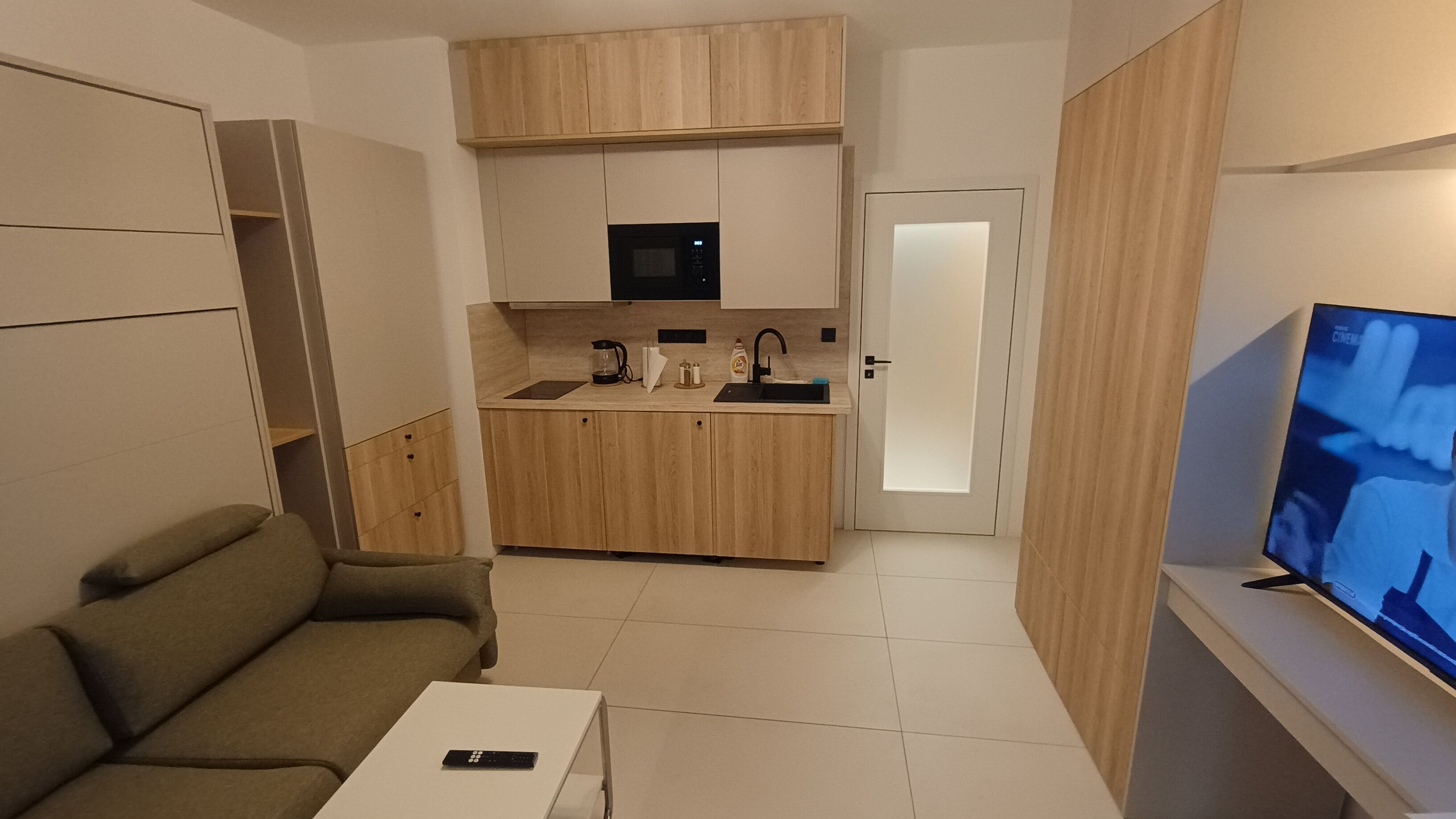 Ett kompakt bostadsutrymme med ett litet kök, en soffa, ett soffbord och en tv.