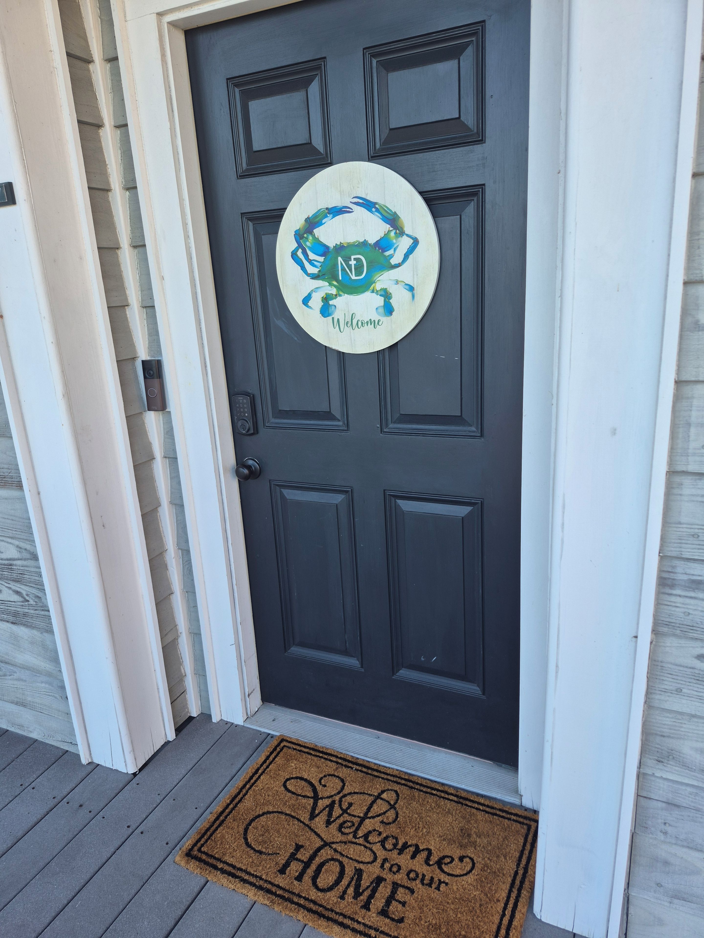 A dark wooden door with a circular welcome sign featuring a crab design and the letters 'ND' above the word 'Welcome'.