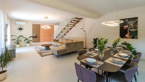 A modern interior with a dining area, sofa, staircase, and potted plants.