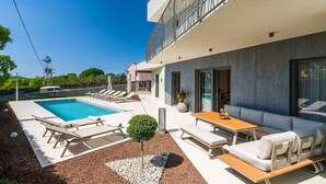 A modern house with a swimming pool, outdoor seating, and a balcony.