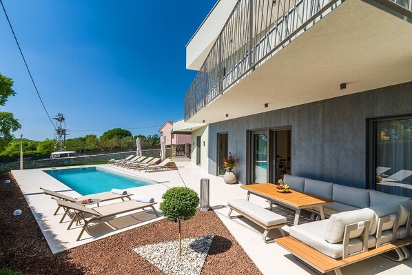 Una casa moderna con piscina, mobiliario exterior y un balcón.