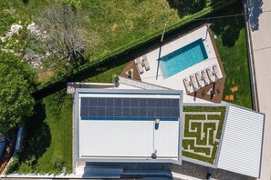 Una piscina en la azotea con un jardín geométrico, un panel solar y una estructura de edificio moderna.