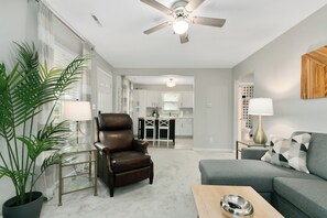 Ein Wohnzimmer mit Ledersessel, grauem Sofa, Couchtisch und Deckenventilator.