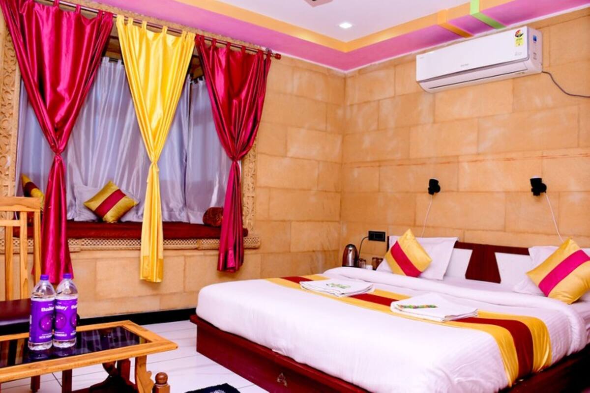 A hotel room with a bed, curtains, an air conditioning unit, a table with bottles, and a window with a view.