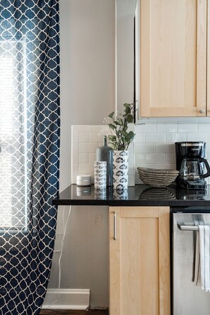 A kitchen with a black countertop, a coffee maker, a vase with plants, and wooden cabinets. - 21 - 2Bd Retreat Near KU Med 21 (Kansas City)