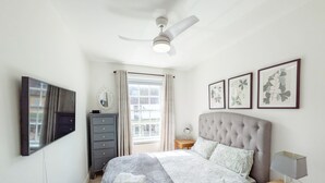 A bedroom with a bed, a ceiling fan, a dresser, a bedside table with a lamp, and framed botanical prints on the wall. - Chichester City Centre Flat -  a flat that sleeps 2 guests  in 1 bedroom (Chichester)