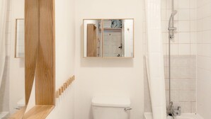 A bathroom with a toilet, a shower, a mirror, and a wooden panel. - Chichester City Centre Flat -  a flat that sleeps 2 guests  in 1 bedroom (Chichester)
