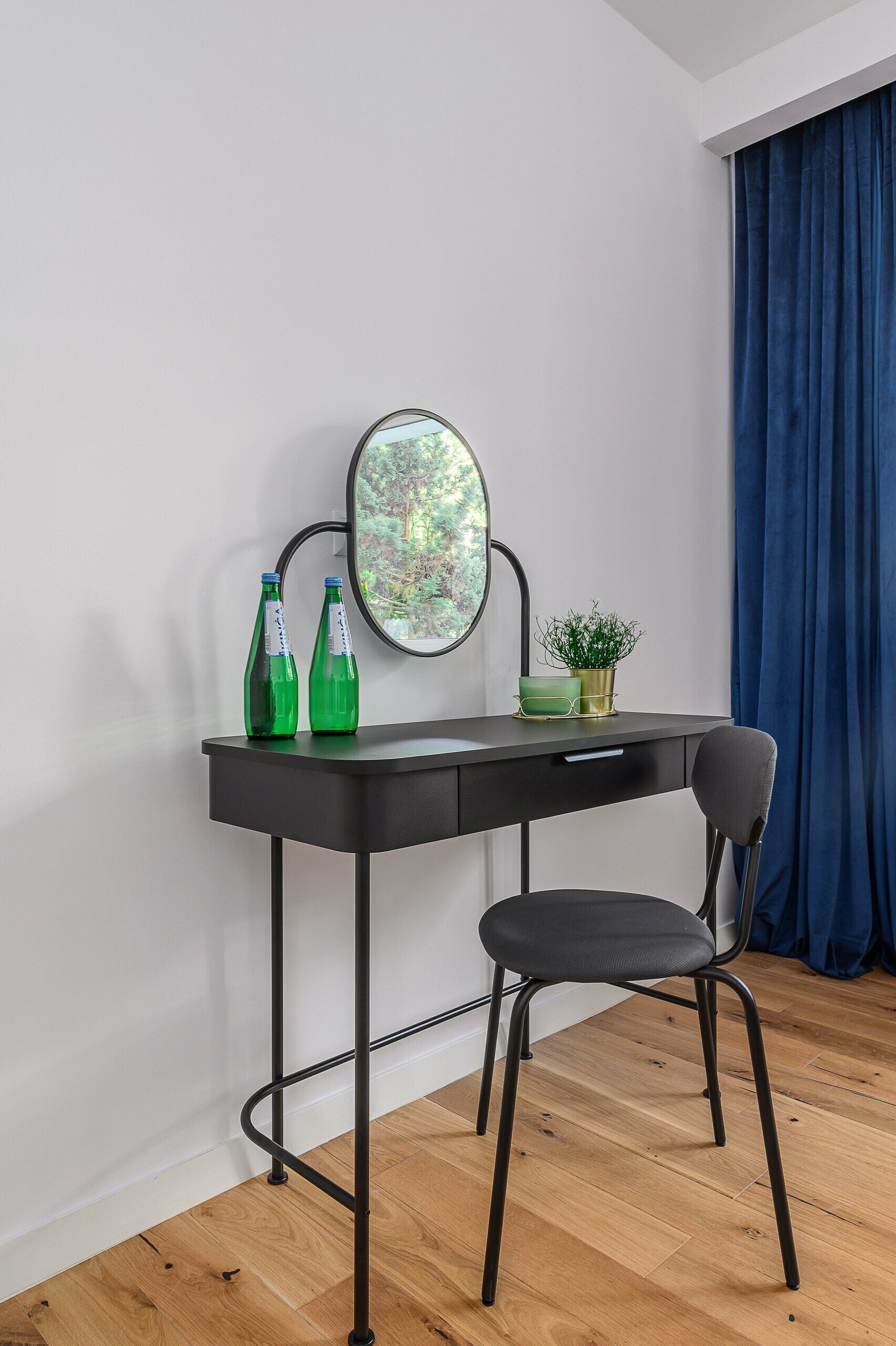 A desk with two green bottles, a small potted plant, and a mirror.