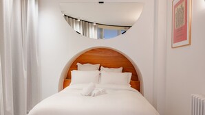 A hotel room with a bed, white curtains, a round mirror, and a framed picture on the wall. - Babylon Montmartre (Paris)