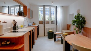 A modern kitchen with a central island, built-in appliances, and a view through large windows. - Babylon Montmartre (Paris)