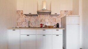 Eine Küche mit weißen Schränken, einer Edelstahl-Dunstabzugshaube, einer Kaffeemaschine und einem weißen Kühlschrank.