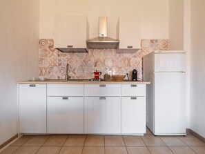 A kitchen with white cabinets, a stainless steel range hood, a coffee maker, and a white refrigerator. - Fortuna by Interhome (Villasimius)