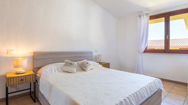 Ein Schlafzimmer mit Bett, Nachttischen, einer Lampe, einem Fenster mit Vorhängen und einer Deckenleuchte.