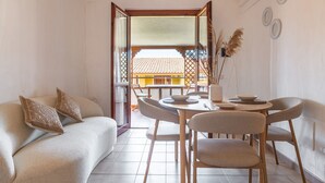 Ein modernes Wohnzimmer mit Sofa, Esstisch, Stühlen und Blick auf ein traditionelles Gebäude durch eine offene Tür.