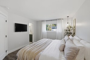 A bedroom with a bed, a TV, a window with curtains, and a plant. - Family Get Away Fireplace Near Columbia River 4 Bedroom Home (Vancouver)
