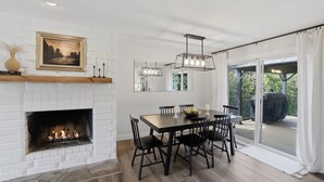 A dining area with a fireplace, a table with chairs, a chandelier, and a view through a glass door. - Family Get Away Fireplace Near Columbia River 4 Bedroom Home (Vancouver)