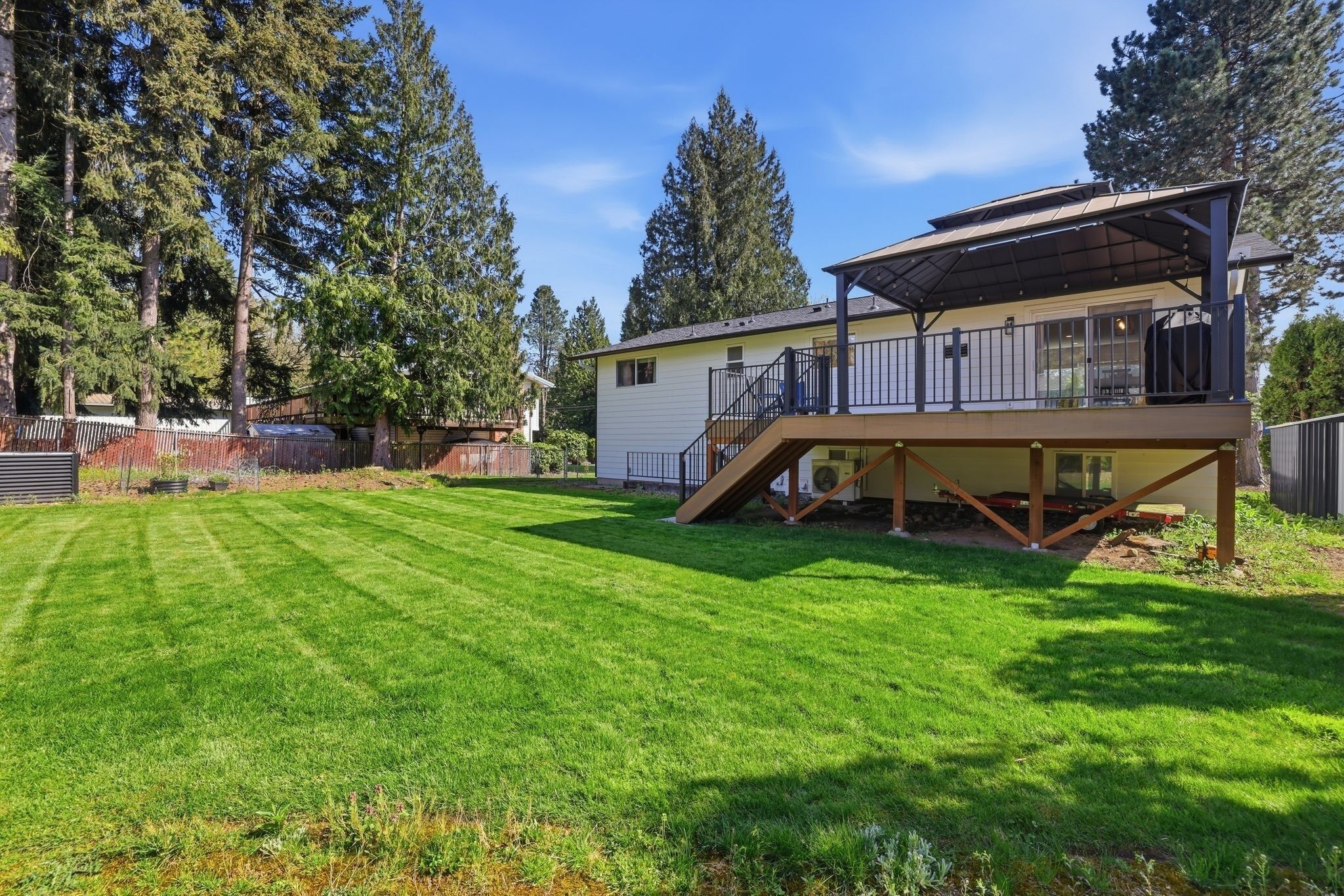 A two-story house with a covered deck, a well-maintained lawn, and tall trees in the background.