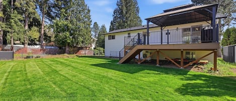 A two-story house with a covered deck, a well-maintained lawn, and tall trees in the background.