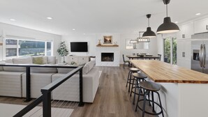 A modern kitchen with a wooden island, bar stools, and a fireplace. - Family Get Away Fireplace Near Columbia River 4 Bedroom Home (Vancouver)