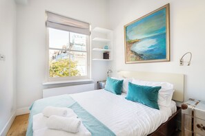 A hotel room with a bed, a window with a view, a painting on the wall, and a bedside table. - Elegant Family Home, Kensington (London)