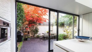 Eine moderne Küche mit einer Schiebetür zu einer Terrasse, auf der sich ein Baum mit roten Blättern und Gartenmöbel befinden.