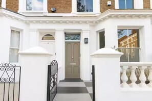 A white townhouse with a beige front door, a small porch, and a gated entrance. - Elegant Family Home, Kensington (London)
