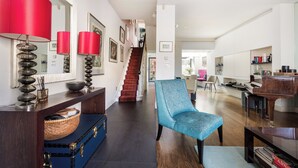 Ein geräumiger Wohnbereich mit Treppe, einem blauen Sessel, einem Klavier und einer roten Lampe.