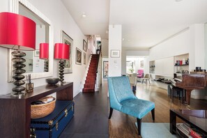 A spacious living area with a staircase, a blue armchair, a piano, and a red lamp. - Elegant Family Home, Kensington (London)