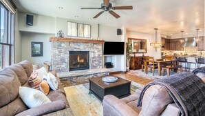 A living room with a stone fireplace, a ceiling fan, and a TV mounted on the wall. - Slopeside Reserve 2 Bedroom Condo (Telluride)