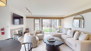 A modern living room with a sofa, armchairs, a coffee table, and a fireplace.
