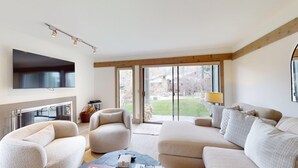 A modern living room with a flat-screen TV, a fireplace, and a large sliding glass door leading to a garden.