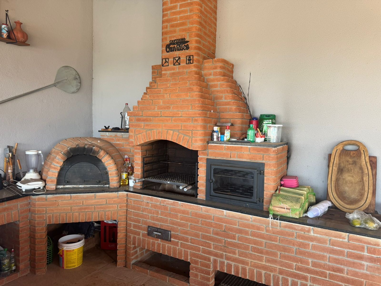 Una cucina esterna in mattoni con forno a pizza, lavello e diversi utensili da cucina.