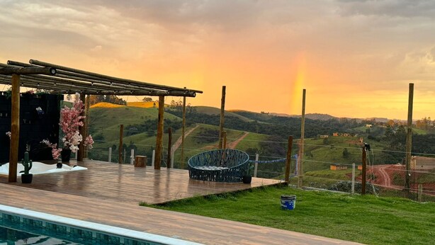 Un espace aménagé au bord de la piscine, avec une pergola, des sièges et une vue sur des collines verdoyantes.